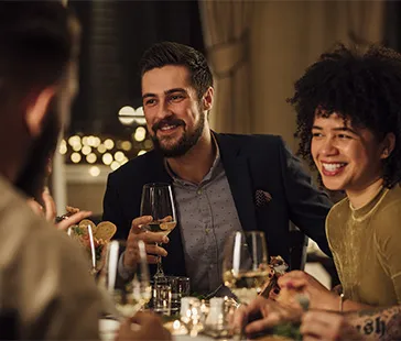 Gruppe speist an einem eleganten Restauranttisch mit Weingläsern, Tellern mit Essen und warmer Beleuchtung.