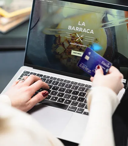 Person nutzt einen Laptop, um eine Restaurant-Website zu durchsuchen, und hält dabei eine Kreditkarte für die Online-Zahlung.
