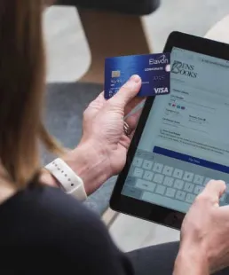 Person hält eine Kreditkarte und gibt Zahlungsdaten auf einer Online-Kassenseite über ein Tablet ein.