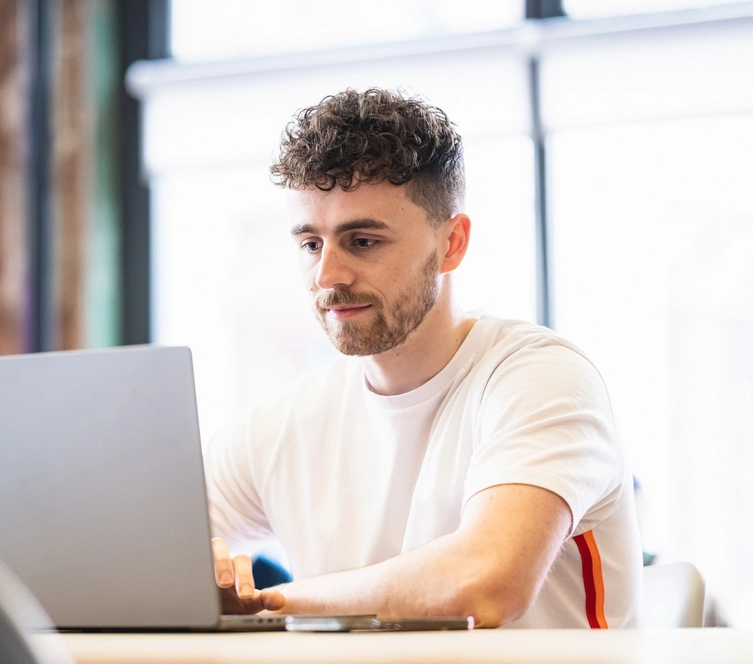Person sitzt an einem tisch und arbeitet an einem laptop in einem hellen raum mit großen fenstern